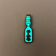 Enamel pin of a Japanese Ramune Soft Drink, a light blue bottle with a white ball towards the top and red Japanese script down the middle. Pin is glowing in the dark.