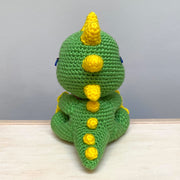 Back view of a crocheted sculpture of a chibi Kaiju, green with yellow spikes and nails.