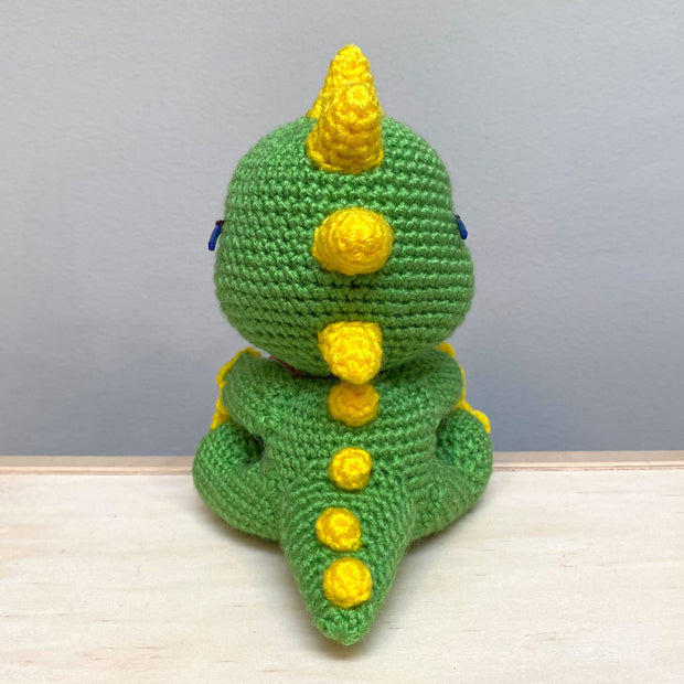 Back view of a crocheted sculpture of a chibi Kaiju, green with yellow spikes and nails.