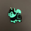 Enamel pin of a Japanese dog figure, white with black accents and wearing a blue and red flower patterned wrap. Pin is glowing in the dark.
