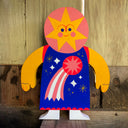 A colorful wood cut of a star-shaped character with a blue and red outfit, presented on a wooden surface.