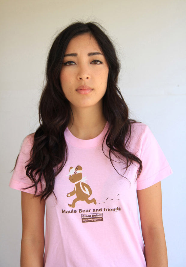 Person wearing pink t-shirt. Illustration of brown bear in a hiking outfit. Grass scatters behind as it walks. Text says Maule bear and friends.