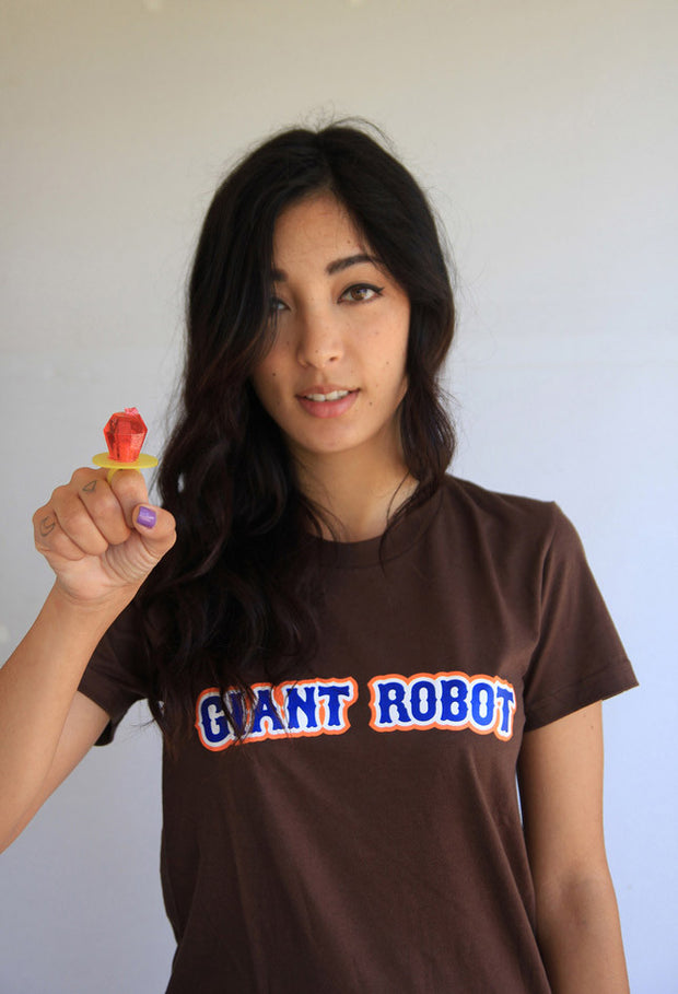 Person wearing brown t-shirt. Front of t-shirt has bold blue text across chest that says giant robot. Text is outlined in white and orange.