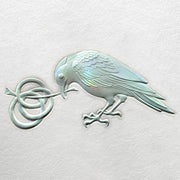 Detail of holographic embossed raven, looking down and holding a swirled, knotted stem.