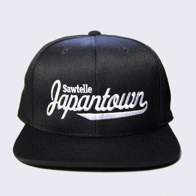 Front of black baseball cap with white embroidery. Sawtelle is stitched in a simple style, while Japantown is stitched in a larger cursive text.