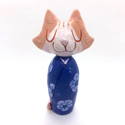 Sculpture of a large headed cartoon style orange and white cat, smiling with its eyes closed. It's wrapped in a blue floral kimono, with no limbs showing and just a tail curled around the back.