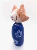 Sculpture of a large headed cartoon style orange and white cat, smiling with its eyes closed. It's wrapped in a blue floral kimono, with no limbs showing and just a tail curled around the back.