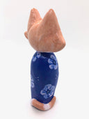 Sculpture of a large headed cartoon style orange and white cat, smiling with its eyes closed. It's wrapped in a blue floral kimono, with no limbs showing and just a tail curled around the back.