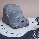 Wooden sculpture of a large whittled sleeping bear, laying on the shore of a lake. A sculpted salmon pops out of the water. Piece is white, black and grey.