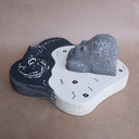 Wooden sculpture of a large whittled sleeping bear, laying on the shore of a lake. A sculpted salmon pops out of the water. Piece is white, black and grey.