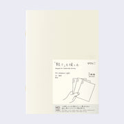 Cream colored blank cover journal within packaging with a cream insert that has Japanese writing and an illustration of a hand holding 3 notebooks.