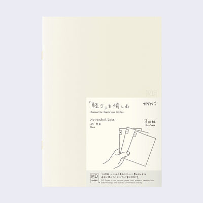 Cream colored blank cover journal within packaging with a cream insert that has Japanese writing and an illustration of a hand holding 3 notebooks.