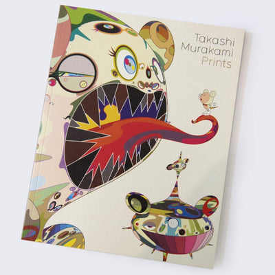 Cover of "Takashi Murakami Prints" book, an abstract Murakami DOB character with many colorful eyes and patterns, sharp dark teeth and a red swirling tongue sticking out. A small character stands on the tongue, with an abstract floating ship like character below.