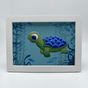 Painting of a cartoon style sea turtle, with a blue shell back. It is submerged underwater with other small fish and kelp forests. Piece is framed in thick white wooden frame.