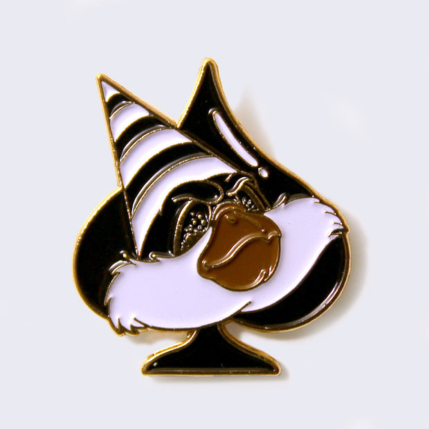 Enamel pin of a fluffy faced creature with a brown snout, and a black and white striped triangle cap. Character is over a black spade.