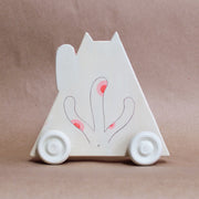 Back view of triangular wooden die cut sculpture of a maneki, a Japanese cat with one paw raised up. It has 3 tails. Wooden sculpture is on wooden wheels.