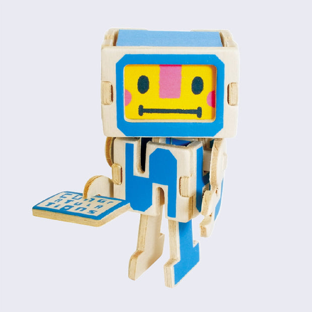 Robot like figure made out of thin wood pieces, assembled like a puzzle. It has a yellow screen for a face and blue color accents. It holds a small flat card that reads "congratulations"