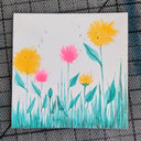 Drawing on white paper of a series of simple pink and yellow flowers, shaped like dandelions, growing out of the ground alongside several blades of bluish green grass.