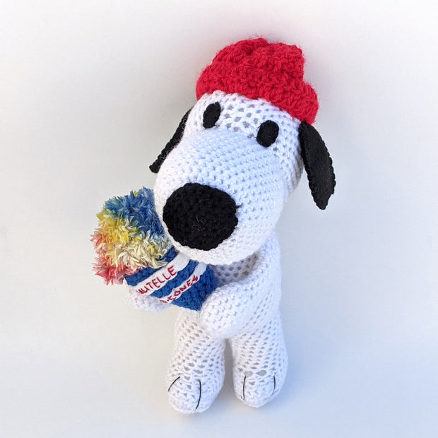 Crocheted plush of Snoopy, wearing a red beanie and holding a knit rainbow colored snowcone.
