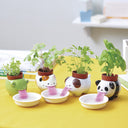 Series of small ceramic animal planters with large pink tongues, extended into a small bowl of water in front of them. Various greenery grows out of their backs.