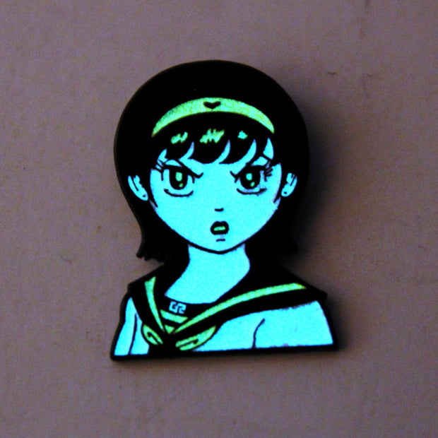 Enamel pin of an illustrated manga girl bust with an angry expression glowing in the dark.
