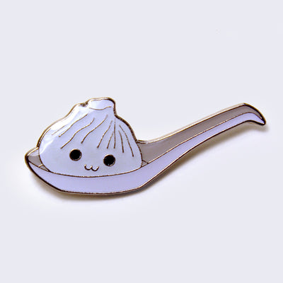 Enamel pin of an illustrated soup dumpling in a large ramen spoon. Dumpling has a smiling face.