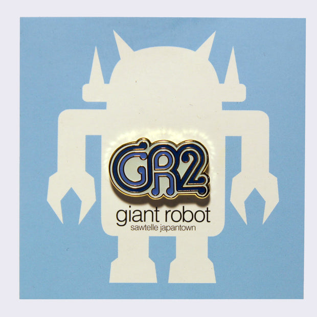 Enamel pin of "GR2" written stylistically in blue with gold and white outlined accents on a blue backing card.