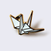 Enamel pin of an origami crane, white with gold accents.