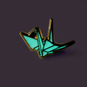 Enamel pin of an origami crane glowing in the dark.