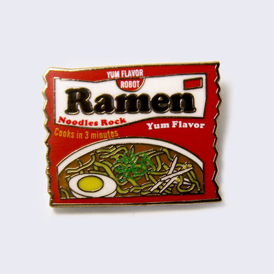 Enamel pin of a red instant ramen packet. Package has "Yum Flavor" written on it under the inital logo.