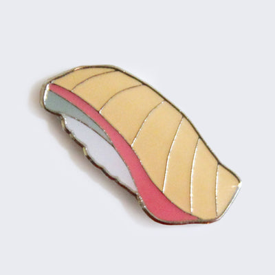 Enamel pin of a piece of yellowtail nigiri. A piece of light orange sushi with a pink side sit atop white rice.