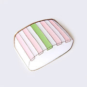 Enamel pin of a white suama mochi treat, with a green stripe in the middle and two pink stripes on either side.