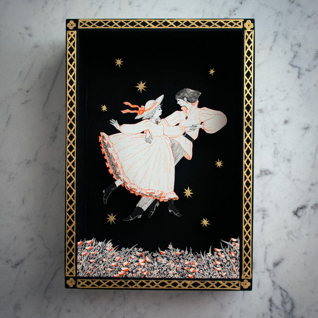 Shadowbox like illustration of a couple, dancing together over a bed of flowers. Illustration is done in very fine lines, orange and black on white paper. They are against an all black background with a gold pattern border and some gold stars floating.