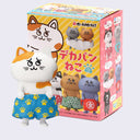 Figurine of a orange and white spotted cartoon cat wearing oversized shorts, standing in front of its product packaging.