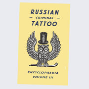 All yellow book cover with a black and white illustrated owl, pattern detail similar to etchings, with a top hat and perched on a crow bar. "Russian Criminal Tattoo" is written in bold black font.