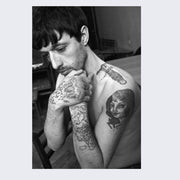 Page example, photograph of a man with clasped hands looking down, his body showing various tattooes.