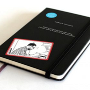 Black book cover with elastic closure. Small illustration of a cartoonist drawing on a desk in bottom left corner. Title and author's name written in thin, all caps white font.