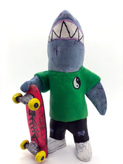 Sculpture of a cartoon style shark wearing a green t-shirt, jeans and white sneakers. He holds a red skateboard with a fishbone design and yellow wheels.