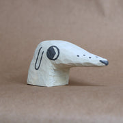 Small whittled wooden sculpture of a dog's head with a very long snout. It has painted on features, and looks off to the side nervously.