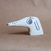 Small whittled wooden sculpture of a dog's head with a very long snout. It has painted on features, and looks off to the side nervously.