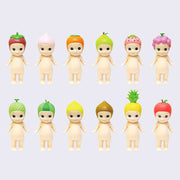 12 vinyl Kewpie babies, standing nude with different fruits atop their heads like hood hats. Options are: strawberry, peach, persimmon, pear, dragonfruit, grapes, melon, watermelon, lemon, durian, pineapple and apple.