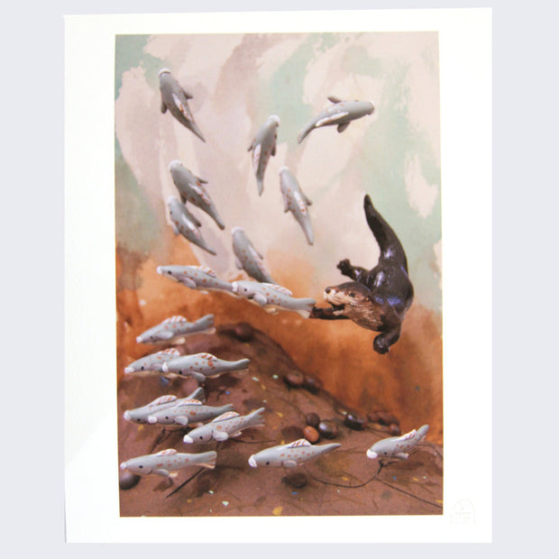 Photograph of a clay and paper diorama. An otter excitedly swims and chases a whole school of fish, which are starting to slowly break their formation.