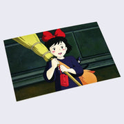 Postcard featuring art from Kiki's Delivery Service of Kiki smiling excitedly and holding up a broom, with a red radio hanging off and a small black cat peeking behind her.