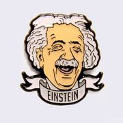 Enamel pin of an illustrated Albert Einstein head, smiling with eyes closed and a scroll banner below that reads "Einstein" in all caps. 