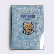 Enamel pin of an illustrated Albert Einstein head, smiling with eyes closed and a scroll banner below that reads "Einstein" in all caps. On a light blue backing card with white doodles, within a decorated plastic case.