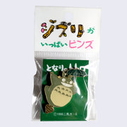 Enamel pin of smiling Totoro balanced with one foot on an acorn and flying with a small, dark green umbrella in a decorated plastic bag.