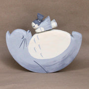 Wooden sculpture of Totoro in profile view, laying on his back with eyes closed, with a little girl with pigtails resting atop his belly. Piece is entirely greyscale and his back is rounded like a wide U shape, instead of laying fully flat.