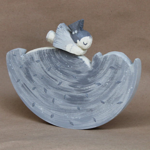 Wooden sculpture of Totoro in profile view, laying on his back with eyes closed, with a little girl with pigtails resting atop his belly. Piece is entirely greyscale and his back is rounded like a wide U shape, instead of laying fully flat.