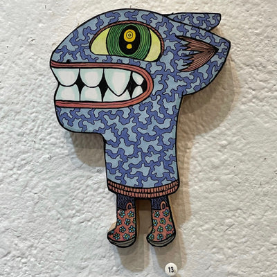 Illustrated wood cut figure of a large headed blue squiggle pattern monster, with large round teeth and a large green eye. It has very small legs and is wearing floral red rainboots.