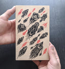 Black and red ink pattern style illustration on exposed wooden panel. The black elements are plant or bug inspired creatures, directioned like in flight. The red elements are like small amoeba creatures.